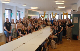 Eine große Gruppe steht um einen Tisch herum und posiert für ein Foto.