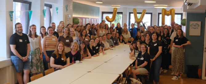Eine große Gruppe steht um einen Tisch herum und posiert für ein Foto.