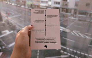 Eine Hand hält einen Flyer vor dem Hintergrund einer leeren Straße.