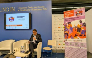 Ein Mann sitzt vor einem blauen Hintergrund und spricht in ein Mikrofon.