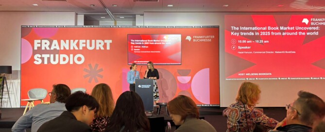 Ein Publikum sitzt vor einer Bühne, am Rednerpult stehen zwei Frauen.