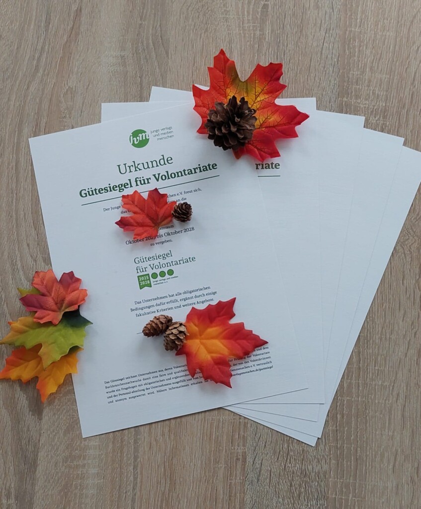 Urkunden "Gütesiegel für Volontariate" liegen auf hölzernem Hintergrund und bunte Herbstblätter und Tannzapfen schmücken die Auslage.