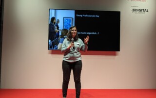 Eine Frau hält ein Mikrofon und steht auf einer Bühne mit rotem Boden.