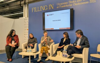 Vier Frauen und ein Mann sitzen vor einer blauen Wand. Eine Frau spricht in ein Mikrofon, die anderen hören ihr zu.